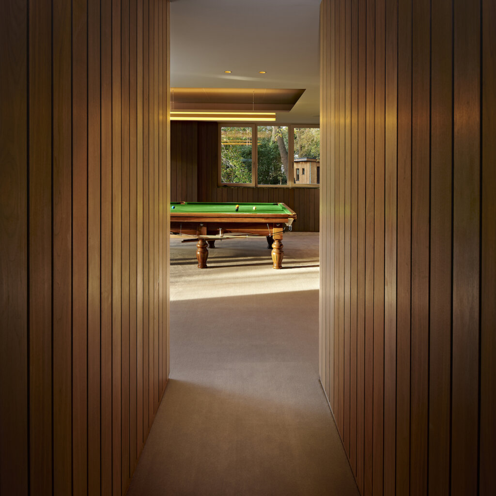 A view down a narrow panelled passageway to a glimpse of a snooker table with tree tops visible through the window behind