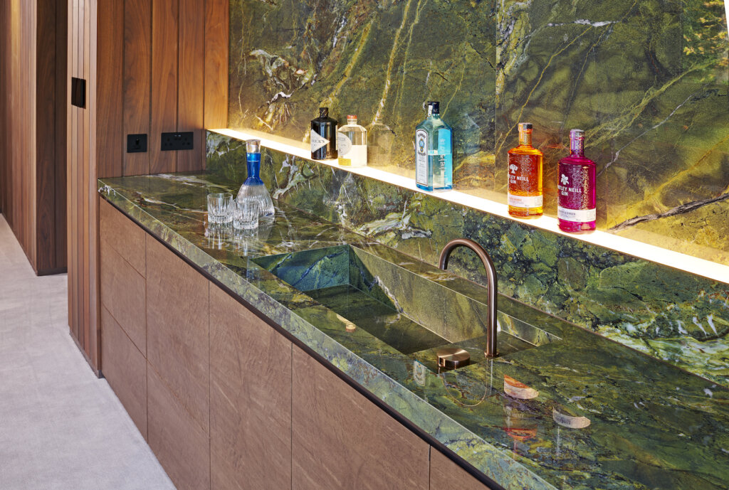 The green marble bar top and sink illustrating the lit shelf with coloured bottles